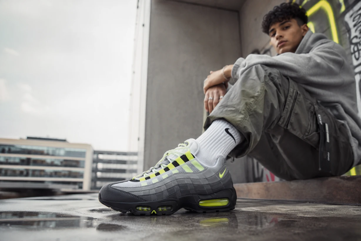 Nike Air Max 95 im urbanen Streetwear-Look mit Neon-Details vor moderner City-Kulisse.