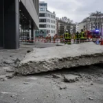 Betonplatte auf Gehweg, Einsatzkräfte sichern Unfallstelle vor modernem Gebäude in Köln