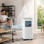 Entspannter Mann im Wohnzimmer neben mobiler Klimaanlage ohne Abluftschlauch im Sommer bei Hitze da.